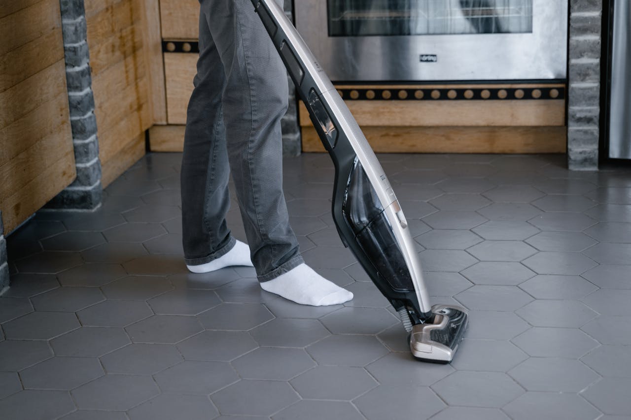 A person cleaning a tiled floor with a modern vacuum cleaner indoors.
